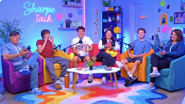 All six Sharpe Family members seated at microphones in the blue and pink Sharpe Talk studio